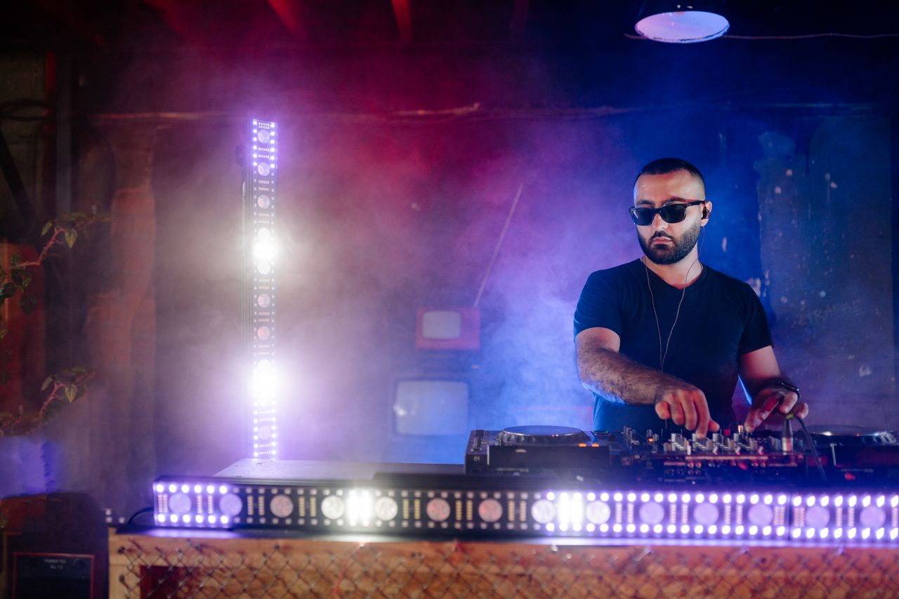 Crafting Captivating Headlines: Your awesome post title goes here A DJ wearing sunglasses mixing music on a deck with vibrant lights and smoke in an indoor club.